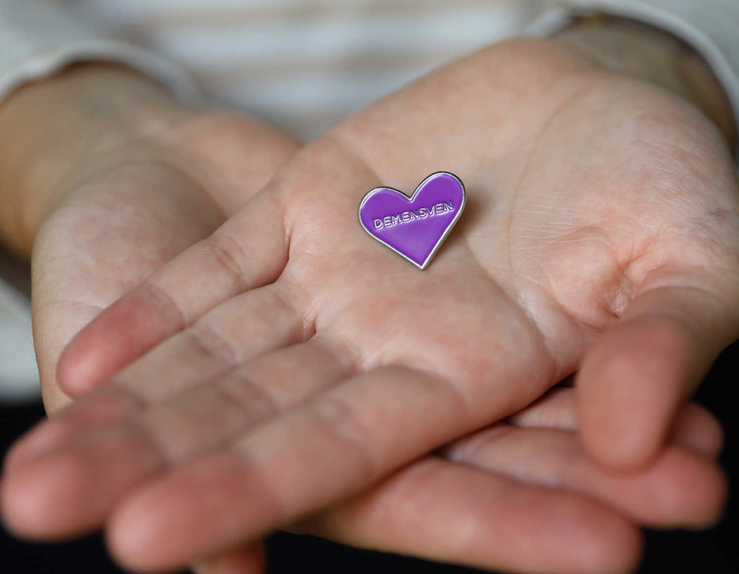 Nærbillede af to hænder, der holder en broche med demensven symbolet.